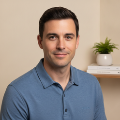 Portrait of Sam Whittaker, a man in his 30s with a warm smile, wearing a slate blue AZURO shirt against a cream background.